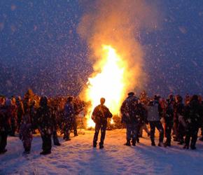 Bonfire at dusk on a snowy field, crowd of people all around